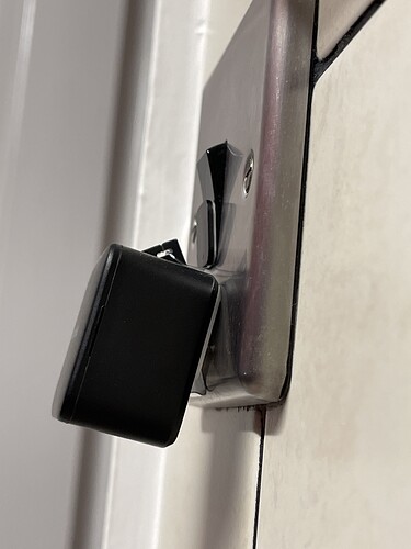 Black SwitchBot on a metal light switch, with a triangular binder clip forcing the SwitchBot to the correct angle.